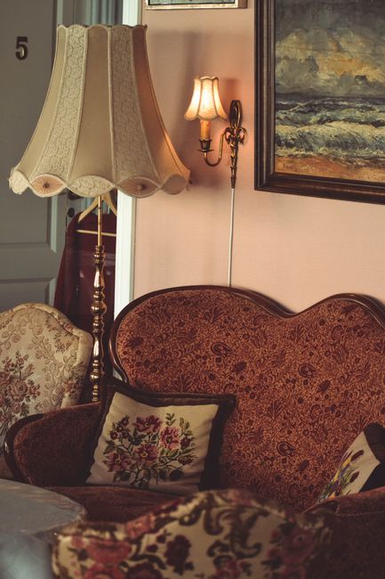 A classic Victorian-style armchair with dark blue leather upholstery and intricately carved wooden frame, positioned against a patterned blue wallpapered wall in a well-lit room. The armchair is place